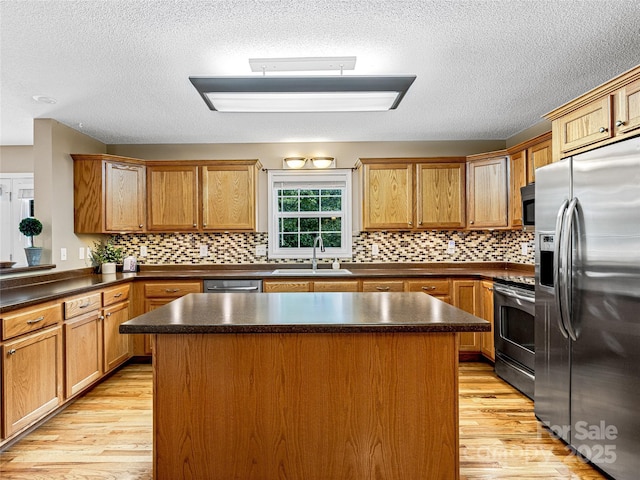 kitchen with light wood-style flooring, a sink, a kitchen island, dark countertops, and appliances with stainless steel finishes