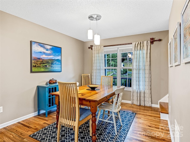 dining area featuring a textured ceiling, baseboards, and wood finished floors