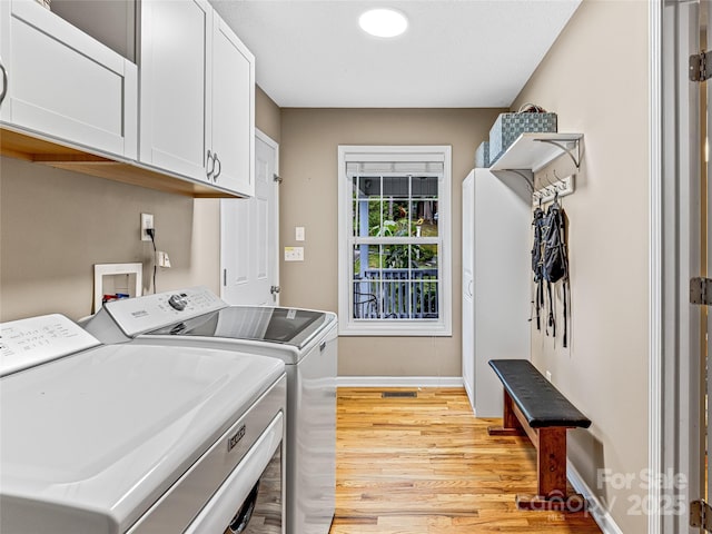 clothes washing area featuring cabinet space, independent washer and dryer, light wood finished floors, and baseboards