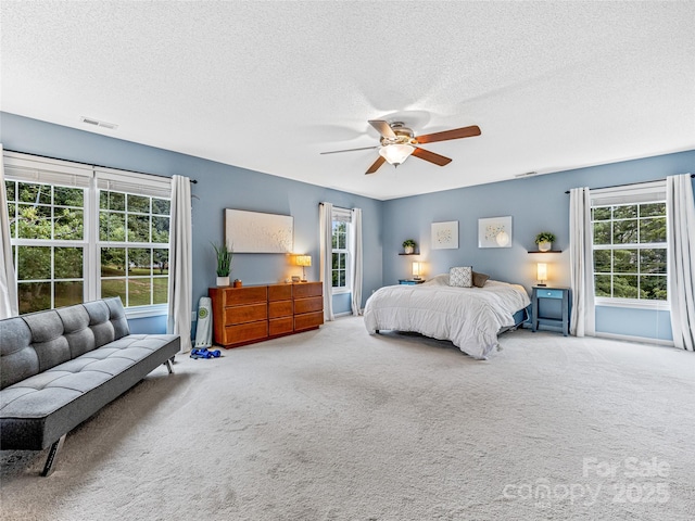 carpeted bedroom featuring a ceiling fan, visible vents, and a textured ceiling