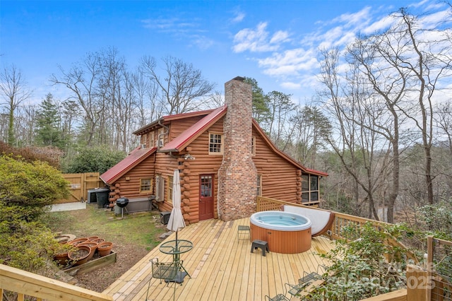 rear view of house featuring a deck, fence, log siding, a chimney, and a hot tub