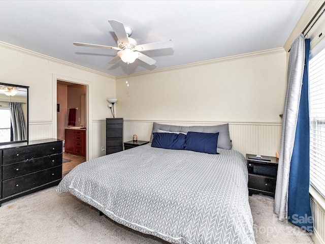 bedroom featuring wainscoting, ensuite bathroom, crown molding, and a ceiling fan