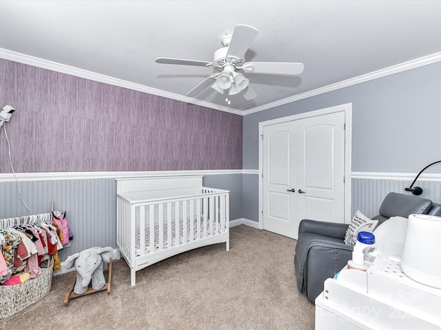 bedroom featuring a crib, a closet, carpet flooring, crown molding, and ceiling fan