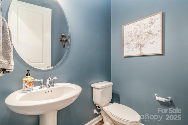 half bathroom featuring toilet, baseboards, and a sink