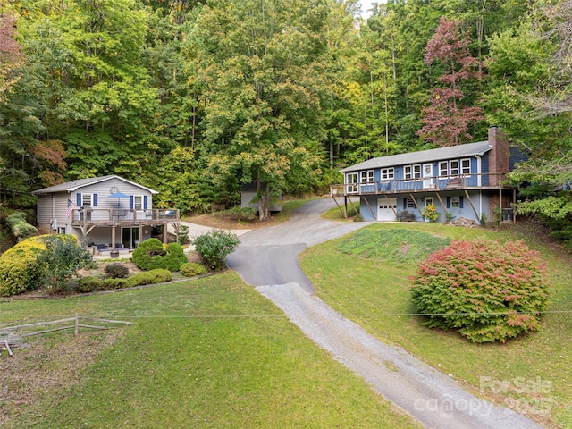 view of front of house with a wooden deck, a front lawn, an attached garage, and driveway