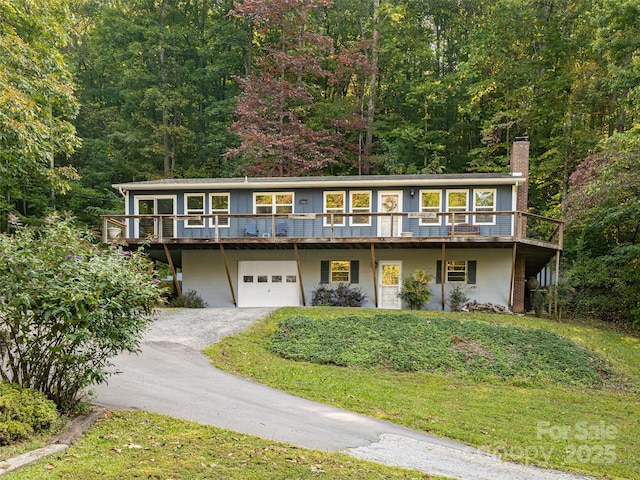 view of front facade with a front lawn, driveway, a wooded view, an attached garage, and a chimney