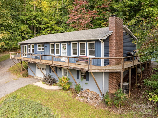 view of front of home with driveway, a chimney, a shingled roof, a front lawn, and a deck