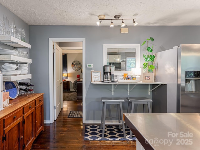 kitchen with a breakfast bar area, stainless steel refrigerator with ice dispenser, dark wood-style flooring, and a textured ceiling