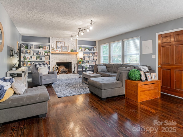 living room featuring a brick fireplace, a textured ceiling, built in shelves, and wood finished floors