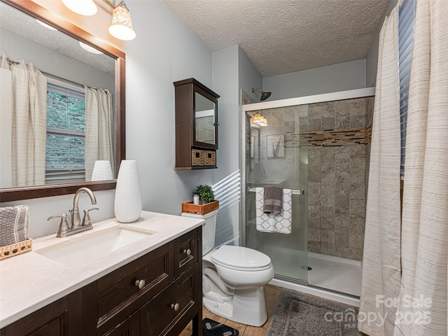 full bath featuring toilet, a stall shower, vanity, and a textured ceiling