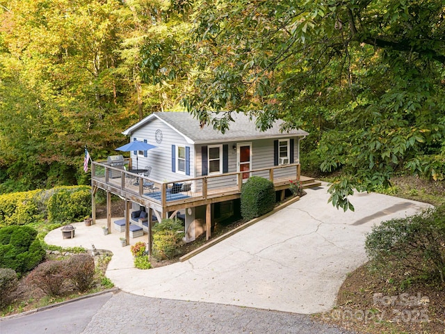 view of front facade featuring a wooden deck, concrete driveway, and a shingled roof