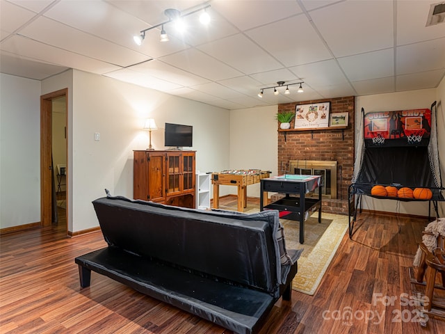 living area with visible vents, a paneled ceiling, a brick fireplace, and wood finished floors