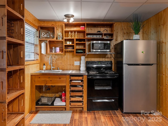 kitchen featuring a sink, stainless steel countertops, wooden walls, and stainless steel appliances