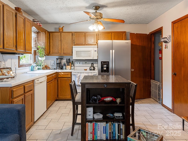 kitchen featuring white appliances, a ceiling fan, a sink, light countertops, and brown cabinets