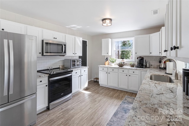 kitchen with visible vents, light wood-style flooring, a sink, white cabinetry, and appliances with stainless steel finishes