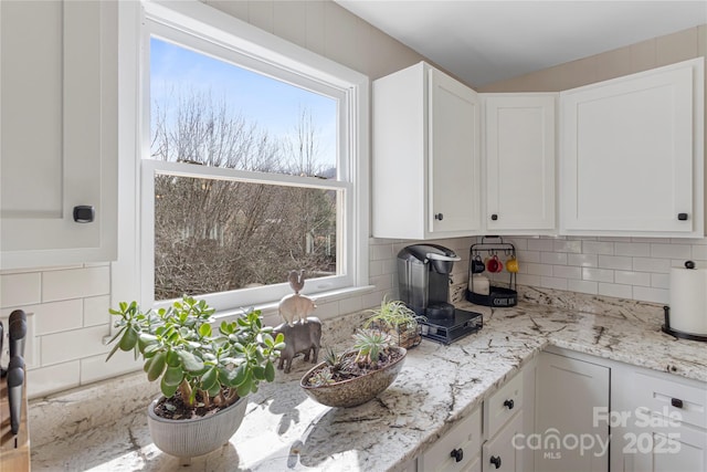 kitchen featuring decorative backsplash, white cabinets, and light stone counters