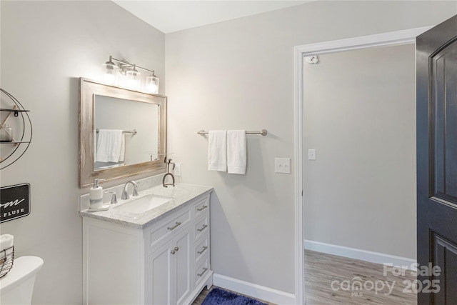 bathroom featuring baseboards, toilet, wood finished floors, and vanity