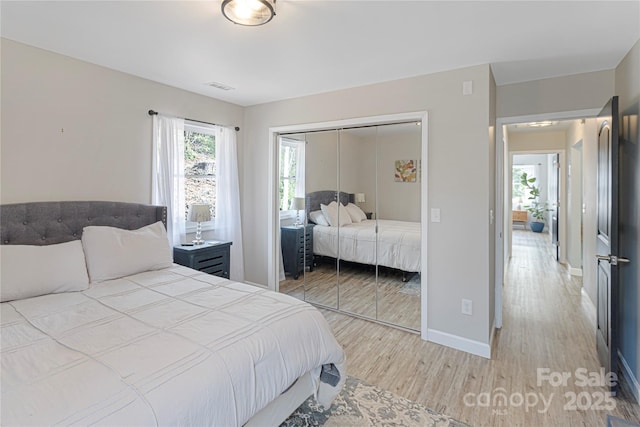 bedroom featuring light wood finished floors, visible vents, baseboards, and a closet