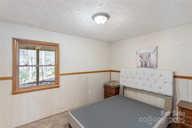 bedroom with a wainscoted wall, wood walls, and a textured ceiling