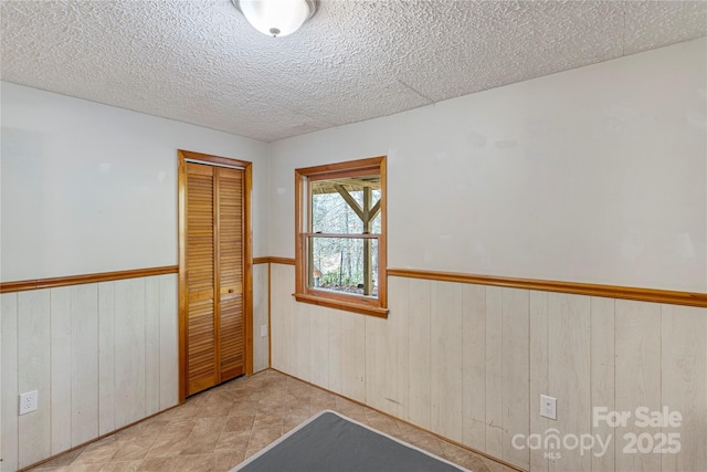 unfurnished bedroom featuring a closet, a textured ceiling, wood walls, and wainscoting