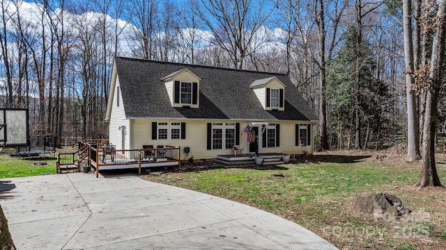 new england style home with a wooden deck, a trampoline, a front lawn, and a shingled roof