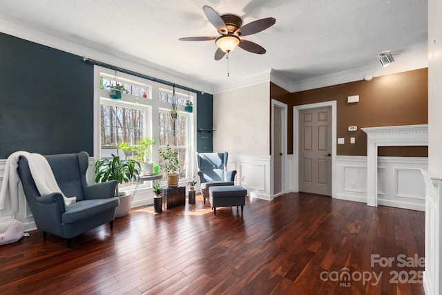 sitting room with a textured ceiling, hardwood / wood-style floors, wainscoting, crown molding, and ceiling fan