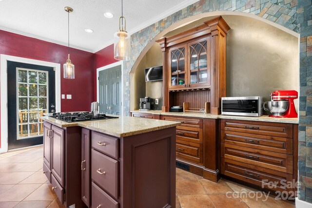 kitchen featuring light stone counters, arched walkways, ornamental molding, hanging light fixtures, and glass insert cabinets