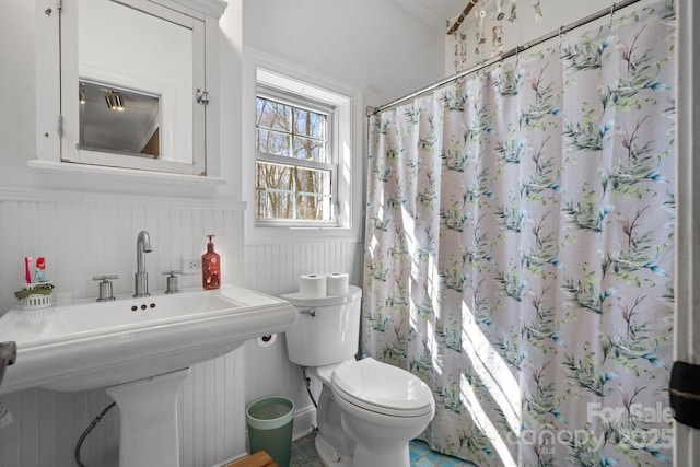 full bath featuring a wainscoted wall, toilet, a shower with curtain, and a sink