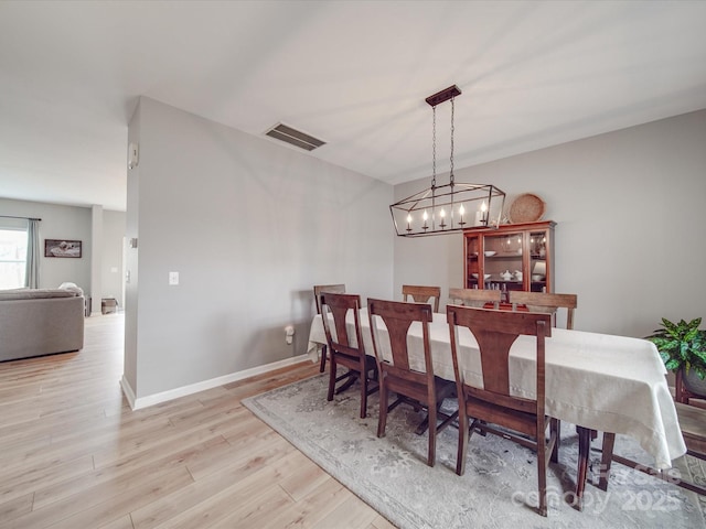 dining space with baseboards, visible vents, light wood finished floors, and a chandelier