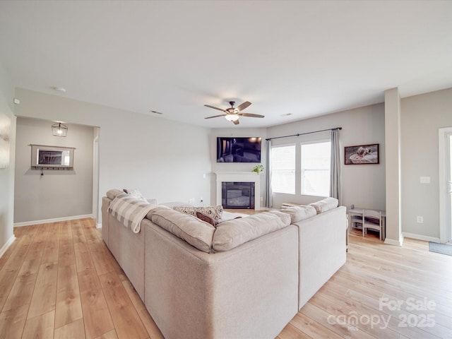 living room featuring a glass covered fireplace, baseboards, light wood finished floors, and ceiling fan