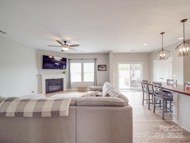 living area with a glass covered fireplace, ceiling fan with notable chandelier, recessed lighting, and light wood-type flooring