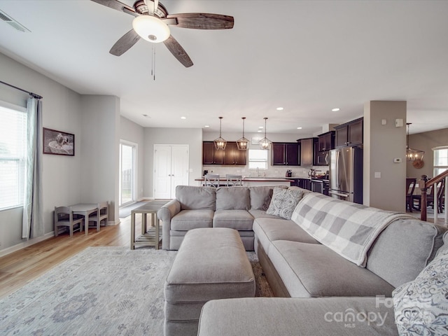 living area featuring visible vents, light wood-style flooring, ceiling fan with notable chandelier, recessed lighting, and baseboards