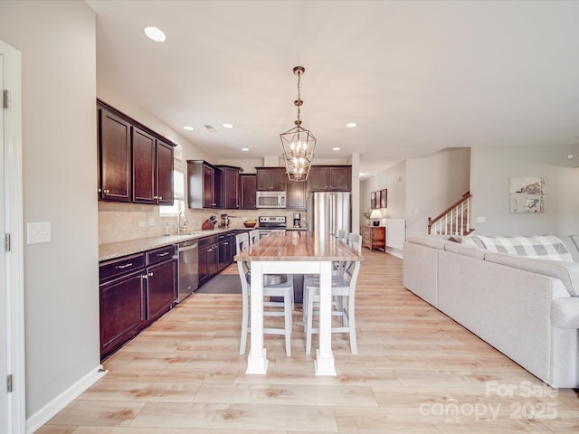 kitchen featuring a sink, open floor plan, appliances with stainless steel finishes, light wood-type flooring, and backsplash