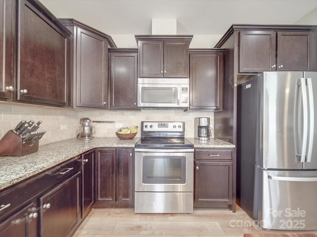 kitchen featuring dark brown cabinets, light stone countertops, tasteful backsplash, and appliances with stainless steel finishes