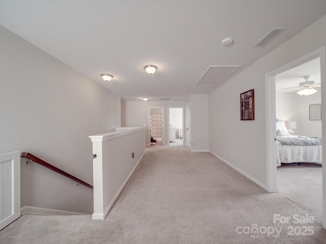 hall with an upstairs landing, visible vents, light colored carpet, and attic access