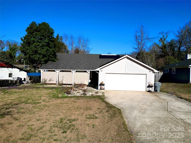 ranch-style house with solar panels, concrete driveway, a front yard, roof with shingles, and an attached garage