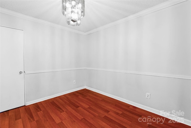 empty room with a textured ceiling, wood finished floors, an inviting chandelier, crown molding, and baseboards