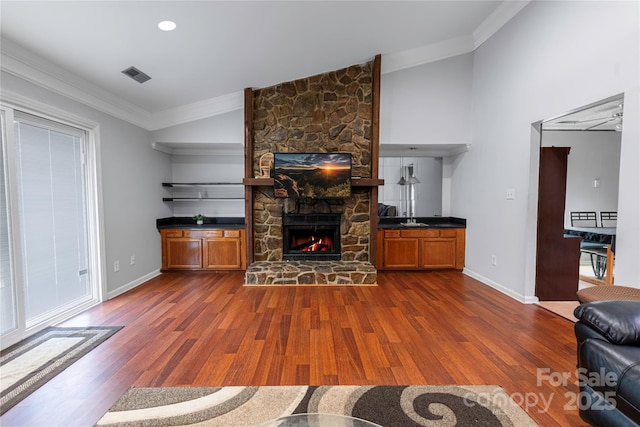 living room featuring dark wood-style floors, vaulted ceiling, crown molding, and a fireplace