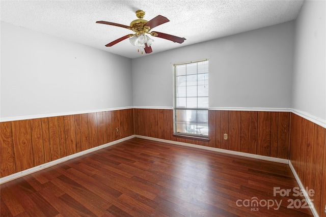 unfurnished room featuring a ceiling fan, wood finished floors, wainscoting, wood walls, and a textured ceiling