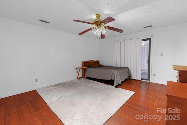 unfurnished bedroom with visible vents, a textured ceiling, wood finished floors, baseboards, and ceiling fan