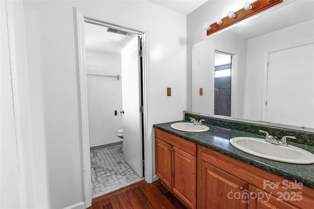 full bath with toilet, wood finished floors, visible vents, and a sink