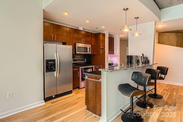 kitchen with a breakfast bar, a peninsula, light wood finished floors, and stainless steel appliances