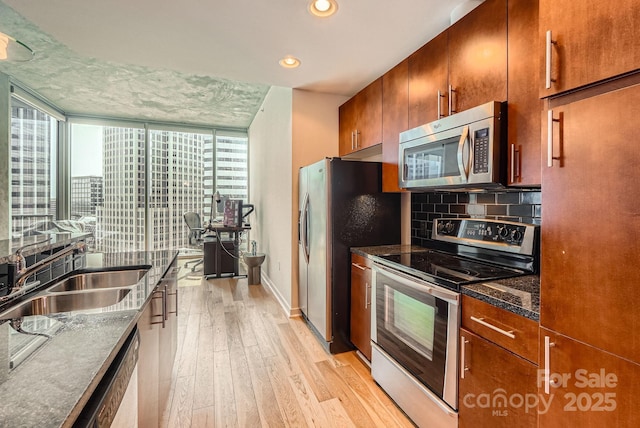 kitchen featuring backsplash, light wood-type flooring, brown cabinets, appliances with stainless steel finishes, and a sink