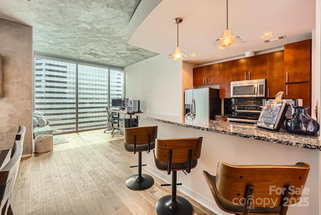 kitchen with visible vents, stainless steel appliances, light wood-style floors, expansive windows, and backsplash