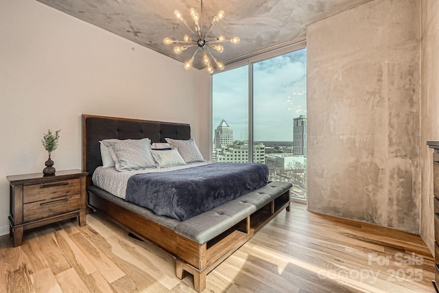 bedroom featuring a wall of windows, wood finished floors, access to exterior, a city view, and a notable chandelier