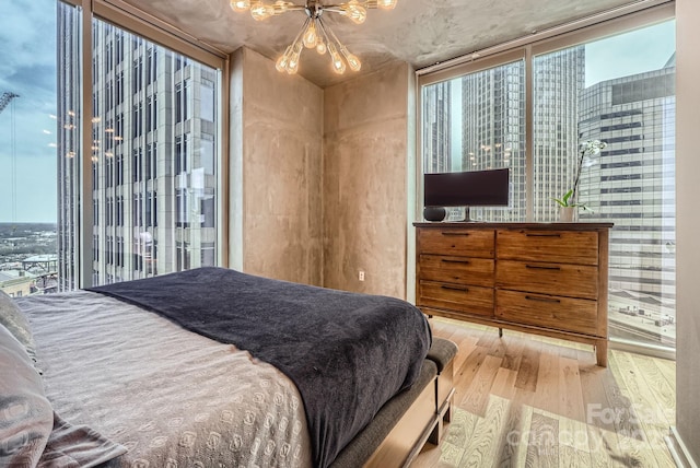 bedroom featuring a wall of windows, an inviting chandelier, and wood finished floors