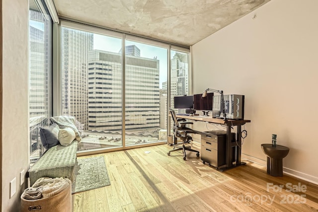 office space featuring floor to ceiling windows, wood finished floors, and baseboards