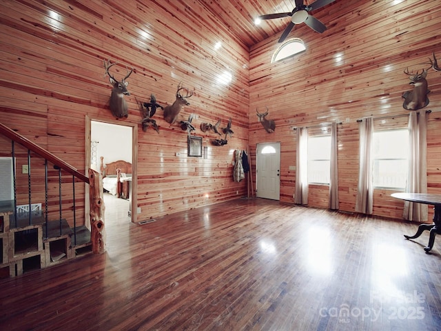 unfurnished living room featuring wooden walls, a towering ceiling, ceiling fan, and wood finished floors