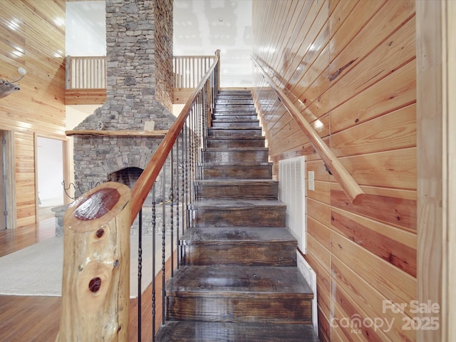 stairs with wood finished floors, a stone fireplace, wood walls, wood ceiling, and a towering ceiling