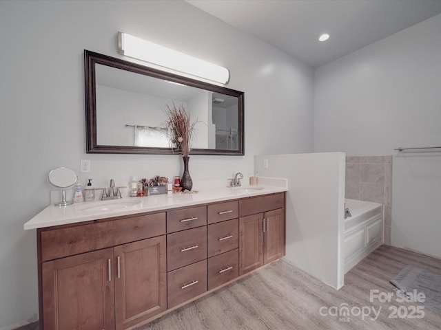 bathroom featuring double vanity, a garden tub, wood finished floors, and a sink